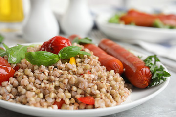 Tasty buckwheat porridge with sausages and vegetables on table, closeup