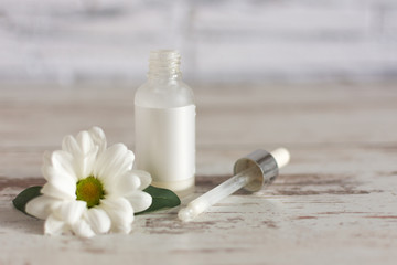 Natural herbal skin care cosmetic with chamomile flower. Facial beauty treatment serum and cream on wooden background.
