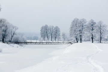 winter landscape with trees and snow, hoarfrost on trees, bridge over the river, path in the snow