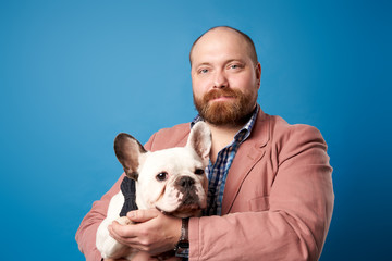 Young male with french bulldog in arms on empty blue background