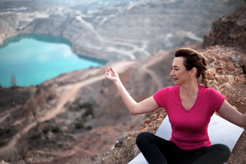 Fototapeta na wymiar 40s years woman dressed sportswear, pink topic and black fitness leggings, sit in yoga pose in harmony herself outdoor against the heart shaped quarry .