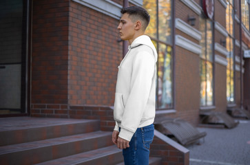 Side view of a white hoodie presentation on a young guy against the background of a brick building.