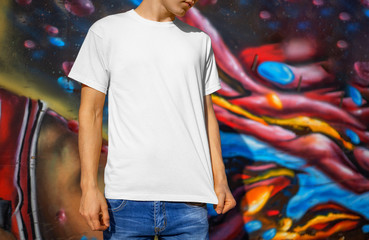 Presentation of a white T-shirt on a young guy, against the background of graffiti, front view.