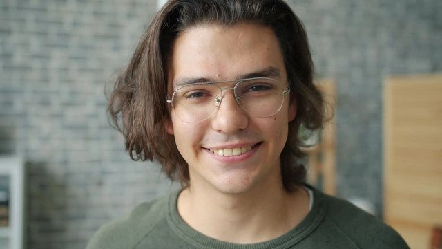 Close-up portrait of good-looking male student in glasses smiling standing indoors in house and looking at camera. People and positive emotions concept.