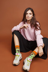 Full length shot of a dark-haired girl, sitting on a floor. She wearing pink sweatshirt, black...