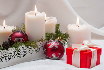 Christmas or New Year card. White burning candles on a light background. Red balls and boxes with gifts. Stand on fir branches