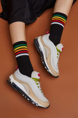 Cropped shot of a girl's foots in white sneakers, lying on a brown background. It is black artwork socks with colored stripes on foots. 