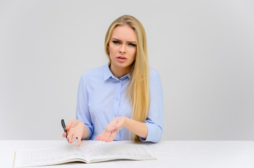 Concept cute model student secretary works sitting at a table. Close-up portrait of a beautiful blonde girl with excellent makeup with long smooth hair on a white background in a blue shirt.