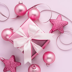 Festive box with a satin bow and pink toy balls on a pastel pink background. Flat style . Holiday concept. Copy space.