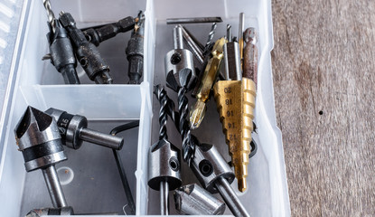Variety of different types of bit drill in transparent orginized box on old wooden background.