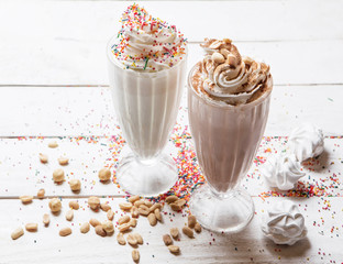 Three sweet milkshakes with nuts, caramel, strawberry and whipped cream at a wooden board on table background.