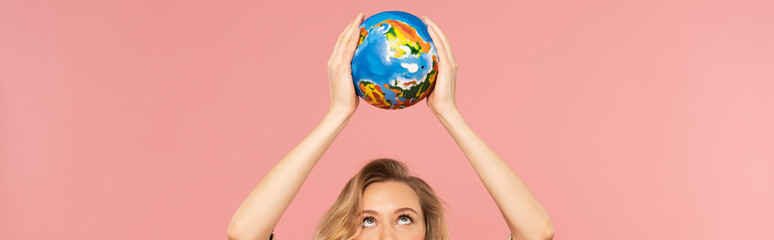 Blonde woman holding globe above head isolated on pink, panoramic shot
