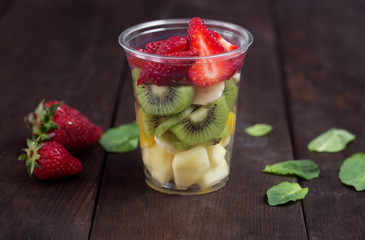 Sliced fruits and berries, arranged in plastic cup