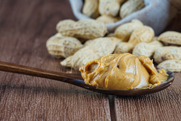 View of a spoon with the peanut butter withe the ground nut in the sack and on the wooden table. selective focus