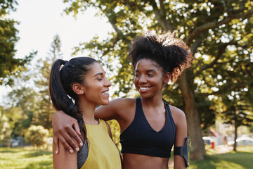 Cheerful young sporty multiethnic female friends hugging eachother and smiling in the park - happy positive friends in the park before exercising