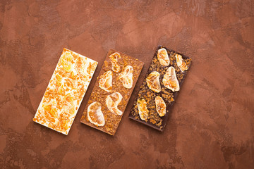 Chocolate whole tiles of various types of milky white dark on a brown background. Flat layout top view. Copy space.