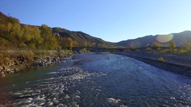 4k aerial drone footage flying low in the afternoon light on the Trebbia river water and the Gobbo bridge near Bobbio in the Piacenza province, nice small italian town.