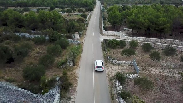 Drone following white car driving in stony fields, Croatia