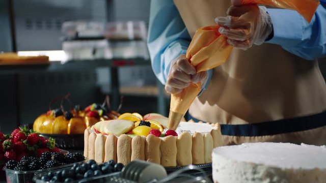 confectioner adds cream to festive cake at table close view