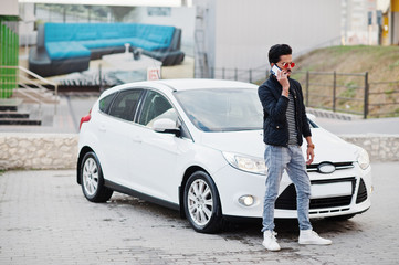 South asian man or indian male wear red eyeglasses stand near his white transportation with mobile phone.