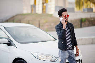 South asian man or indian male wear red eyeglasses stand near his white transportation with mobile phone.