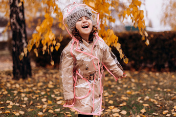 Happy funny child girl wearing transparent raincoat outdoor in autumn. Cheerful girl laughing