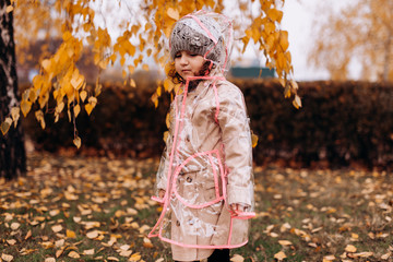 Happy funny child girl wearing transparent raincoat outdoor in autumn.