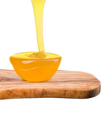 Glass bowl full of honey and falling jet of honey on plank isolated on white