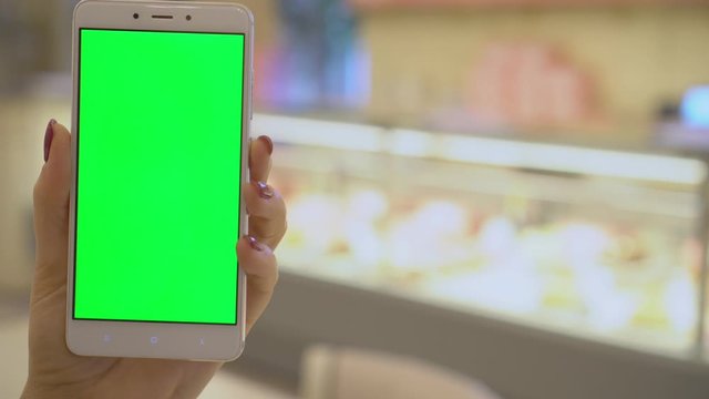 4K Close up of hand holding a smartphone with green screen display in supermarket.