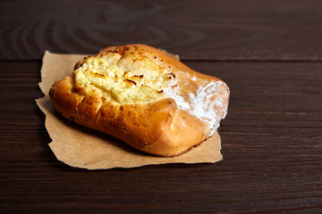 Wheat bun with curd filling on a wooden table, close-up. Bakery, bun with cottage cheese on baking paper on brown background