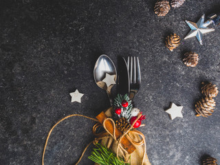 Festive Greeting Card Merry Christmas, Happy New Year, Winter holiday dinner spoon, fork, knife in burlap, decorated with rope, stars. Christmas tree branch, and berry, cone on grey mabrle background
