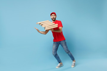 Delivery man in red workwear giving food order pizza boxes isolated on blue background, studio portrait. Professional male employee in cap t-shirt print courier. Service concept. Mock up copy space.