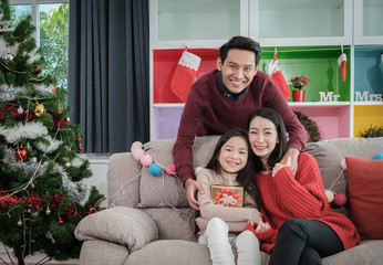 portrait of family with a father mother and daughter holding gift box celebrating Christmas night decorated with Christmas trees on Christmas Day.. - 304674604