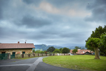 Village, rural landscape at cloudy summer  day, farm buildings with tiled roofs. Road, house and fence, countryside, Atlantic Pyrenees, France. Overcast weather