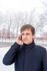 Man standing by the snow covered car and talking on the smart phone