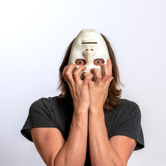 A man covers his face with a white mask upside down and tries to tear it off. The concept of...