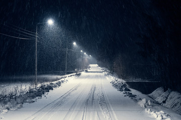 road in the blizzard snow in winter at night. In the light of lamps visible falling snow. - obrazy, fototapety, plakaty