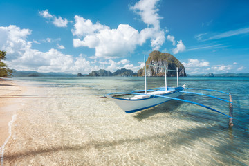 El Nido, Palawan, Philippines. traditional banca boat on sandy beach with crystal clear water on morning island hopping trip. Amazing Pinagbuyutan island in background. Beautiful landscape scenery