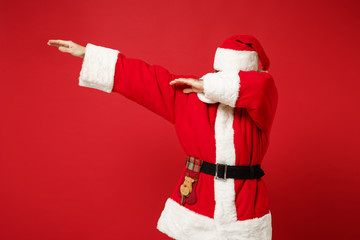 Elderly gray-haired Santa man in Christmas hat posing isolated on red wall background, studio portrait. Happy New Year 2020 celebration holiday concept. Mock up copy space. Showing DAB dance gesture.