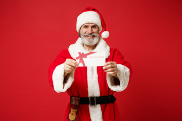 Fototapeta na wymiar Smiling elderly gray-haired mustache bearded Santa man in Christmas hat isolated on red wall background. Happy New Year 2020 celebration holiday concept. Mock up copy space. Holding gift certificate.