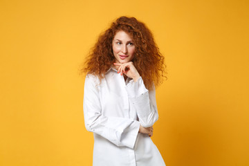 Pensive young redhead woman girl in casual white shirt posing isolated on yellow orange background in studio. People sincere emotions lifestyle concept. Mock up copy space. Put hand prop up on chin.