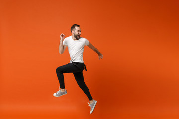 Fototapeta na wymiar Crazy young man in casual white t-shirt posing isolated on bright orange wall background studio portrait. People lifestyle concept. Mock up copy space. Having fun, fooling around, jumping screaming.
