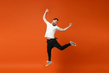 Fototapeta na wymiar Happy excited young man in casual white t-shirt posing isolated on bright orange wall background studio portrait. People lifestyle concept. Mock up copy space. Having fun jumping doing winner gesture.
