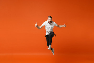 Fototapeta na wymiar Crazy young man in casual white t-shirt posing isolated on orange wall background studio portrait. People lifestyle concept. Mock up copy space. Having fun, fooling around, jumping, showing thumbs up.