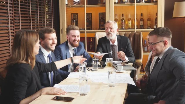 Gray haired general director sitting in big leather chair examining terms of transaction against the wall with collection of alcohol business meeting of top managers