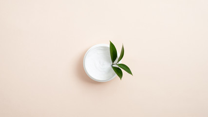 Obraz na płótnie Canvas Jar with white organic cosmetic cream and green leaf on pastel beige background. Minimal flat lay style composition, top view. Skin care and healthcare concept.