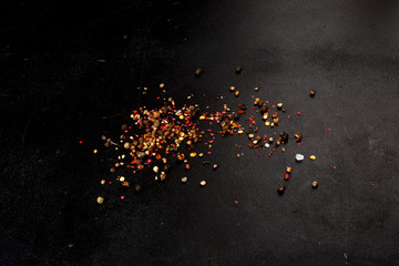 Different types of pepper sprinkled on a black background