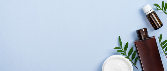 Flat lay cosmetic bottle containers. Top view jar with white face cream, rosemary oil for hair growth, balm shampoo and rosemary leaves on pastel blue background. Natural beauty product concept.