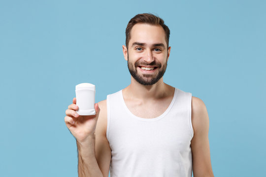 Bearded young man 20s years old in white shirt hold using antiperspirant isolated on blue pastel wall background, studio portrait. Skin care healthcare cosmetic procedures concept. Mock up copy space.