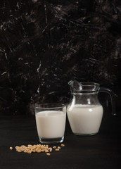 Vegetable milk from pine nuts in a glass and a glass jug on a black background. vertical